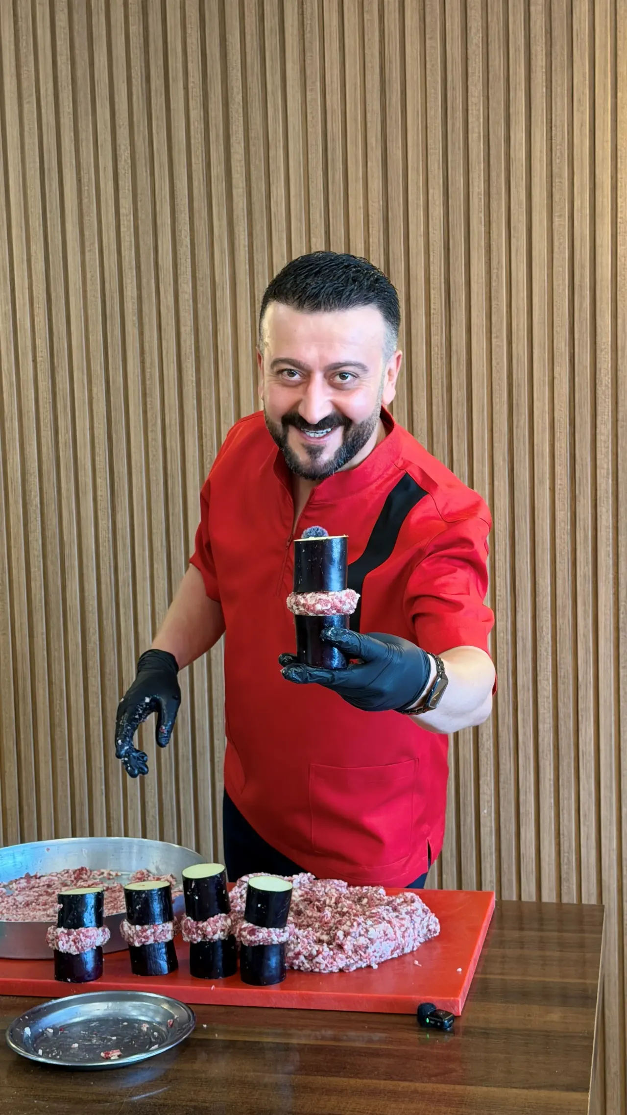 Kırmızı ceketli aşçı, patlıcan ve kıymayla hazırladığı kebabı gösteriyor