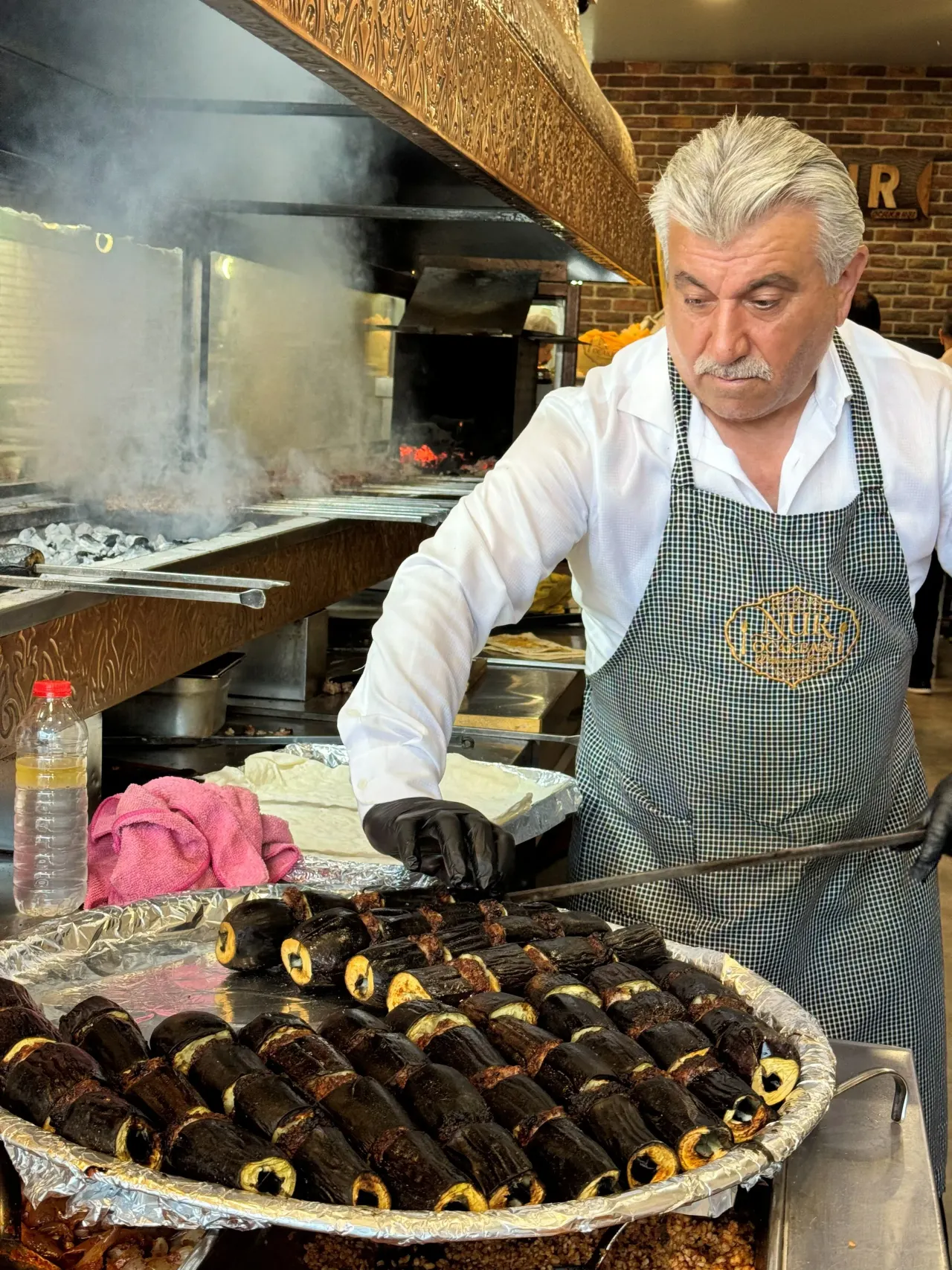 A Nur Ocakbaşı master in an apron preparing a tray of aubergine kebab at the smoking grill