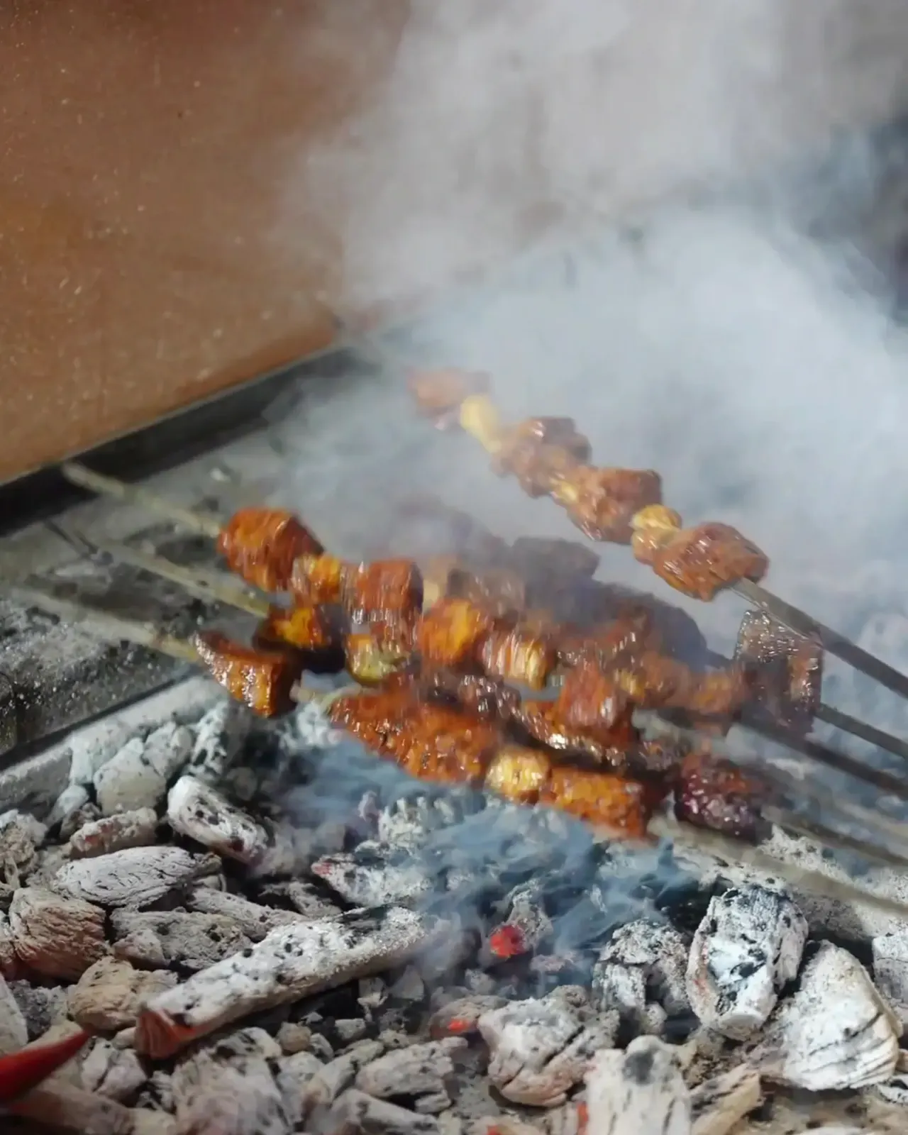 Lamb skewers cooking in smoke over embers on the grill
