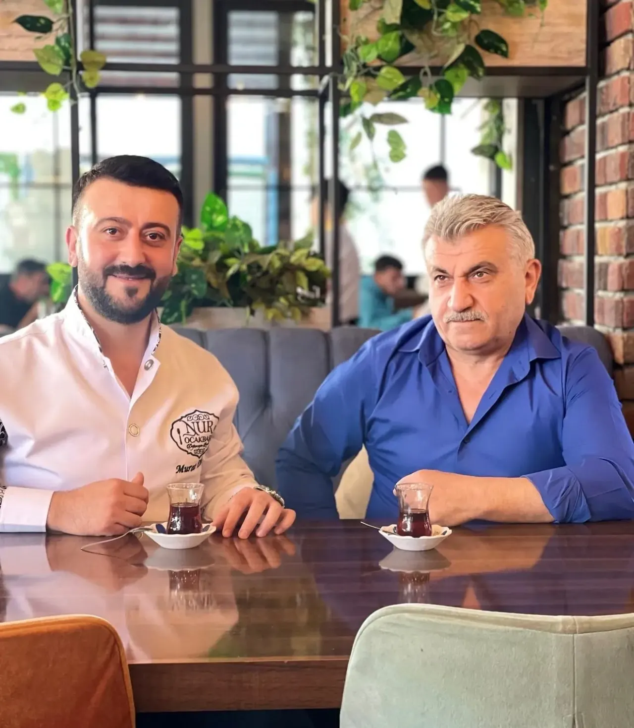 İki kişi restoranın salonunda, çay bardaklarıyla masada oturuyor