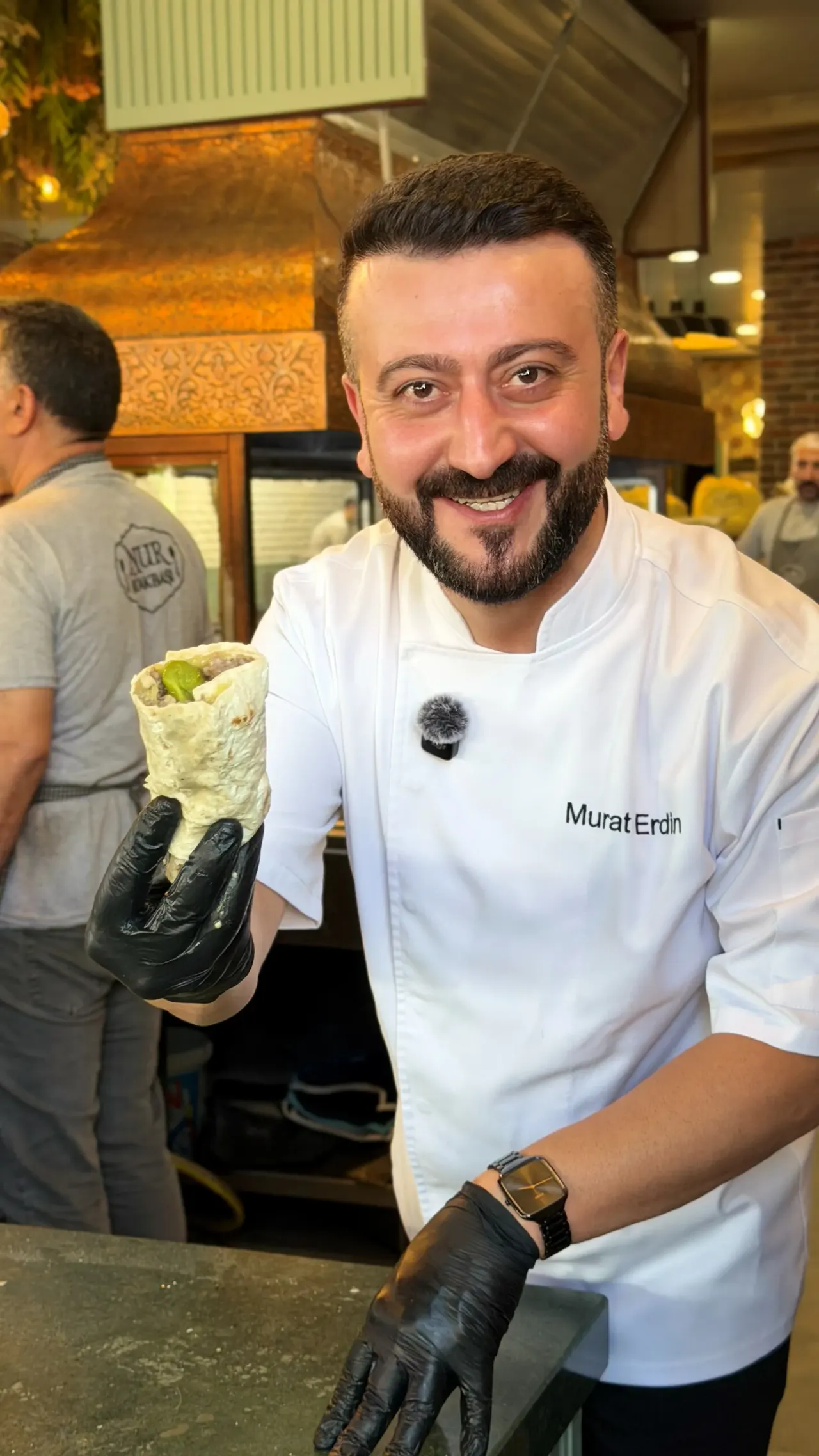 A cook in a white jacket showing a dürüm wrap he made at the grill